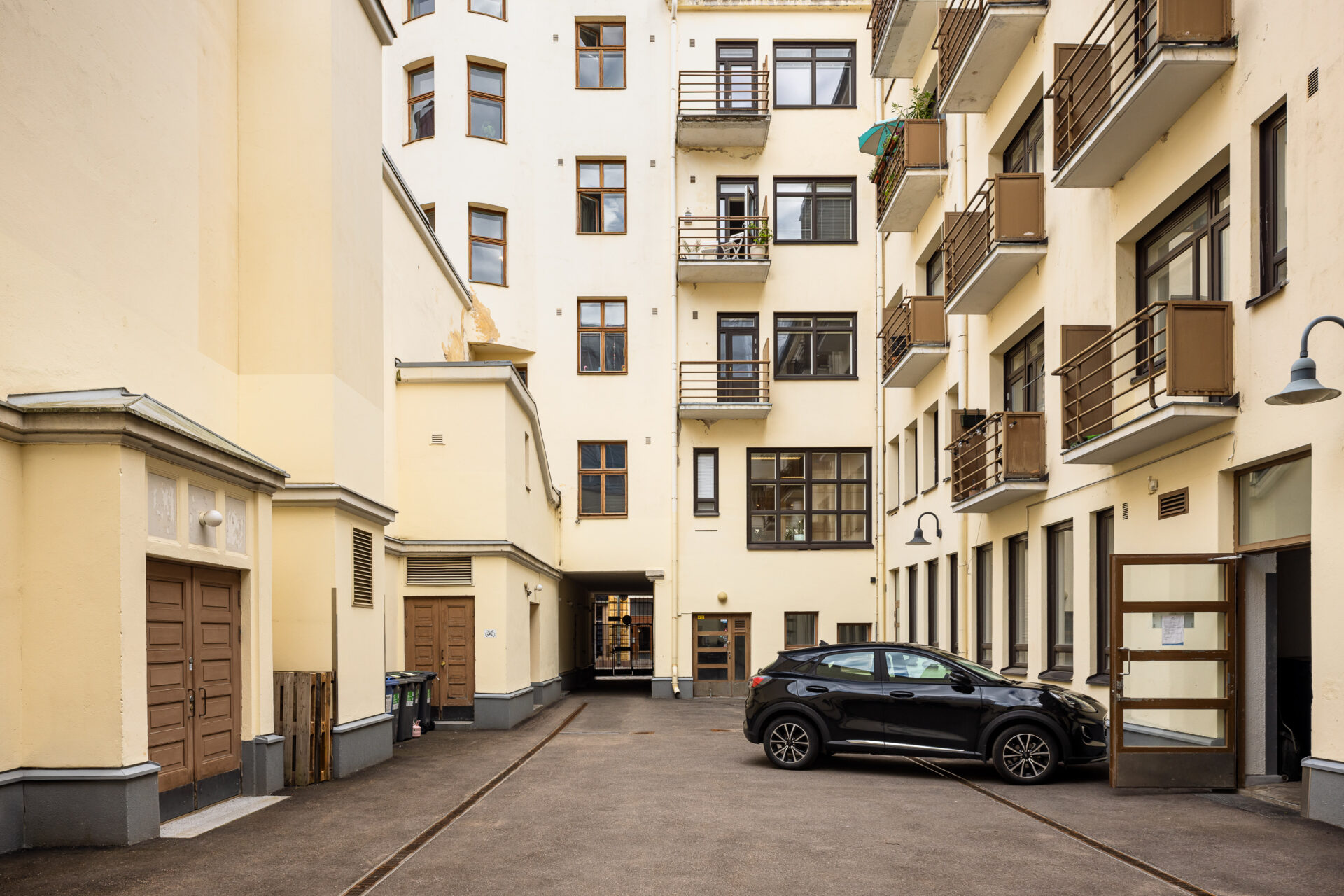 Musta viistoperä oli pysäköity vaaleankeltaisen kerrostalon pihalle, jossa oli useita pieniä parvekkeita.